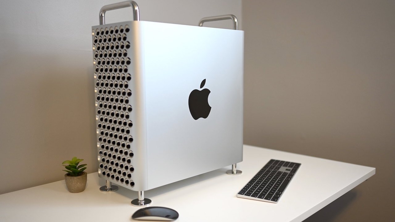 Silver desktop computer with a perforated front and Apple logo, on a white desk, accompanied by a keyboard, mouse, and small potted plant.