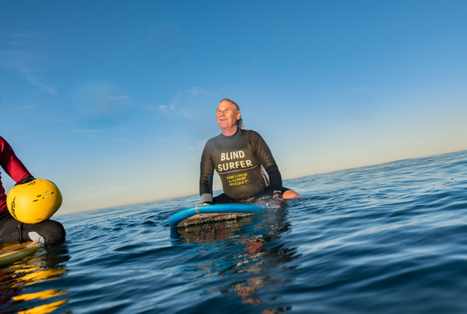Blind surfer Scott Leason waiting for a wave on a surfboard at sea.