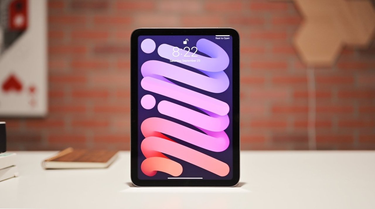 Tablet on a white table with colorful wavy wallpaper, time 8:22, brick wall background, books, and art in the background.