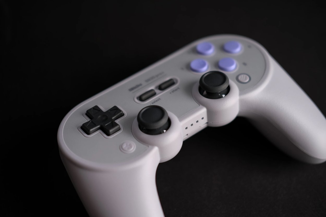 A close-up of a white 8BitDo SN30pro+ Wireless Bluetooth gaming controller against a black background. The controller features a directional pad, dual thumbsticks, and four buttons.