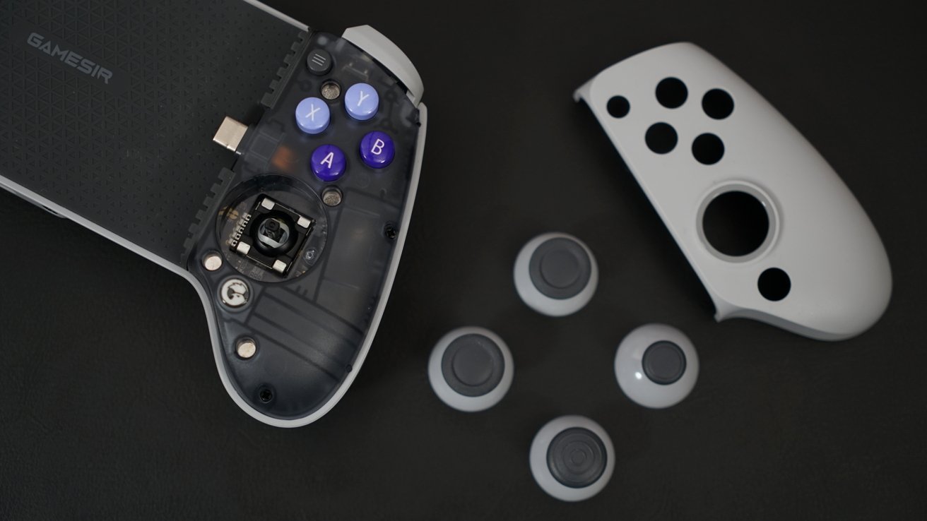 GameSir controller with faceplate removed lies next to its gray faceplate and four joysticks. The transparent plastic on the controller shows internal circuitry.