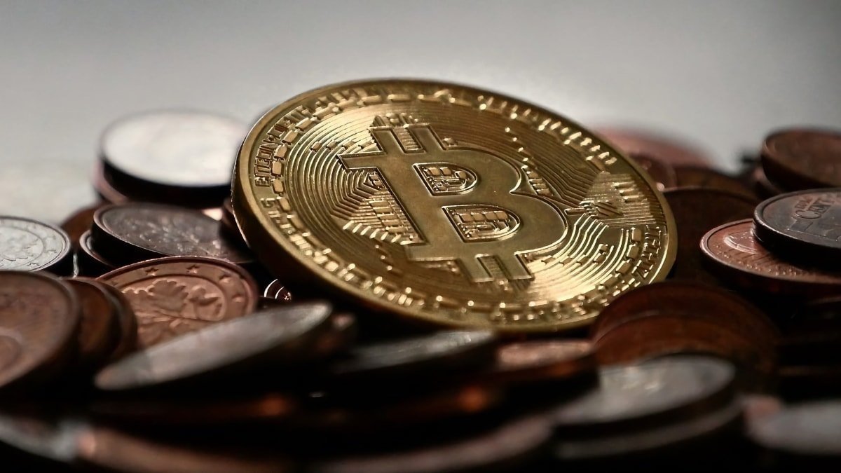 A golden Bitcoin rests on a pile of assorted coins with a blurred background, symbolizing cryptocurrency among traditional money.