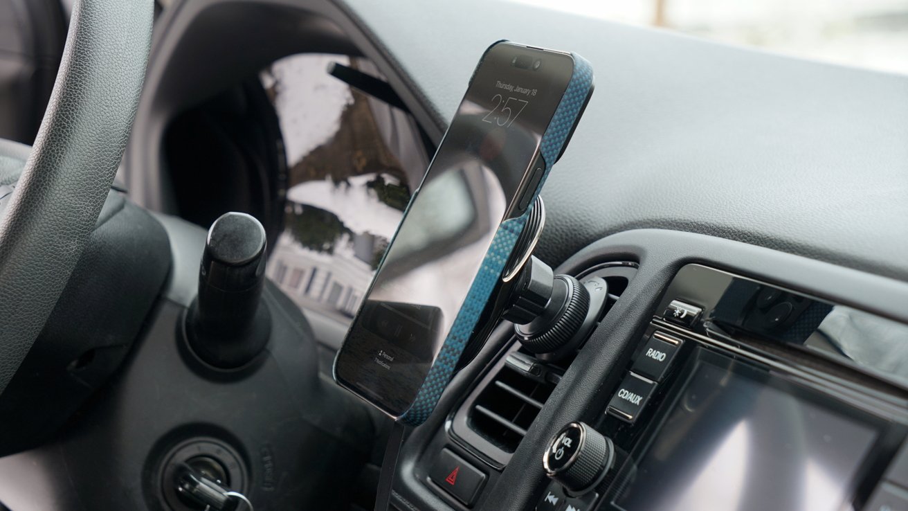 The Pitaka car charger attached to a vent on a black car dash next to an infotainment system. An iPhone is attached with a blue case.