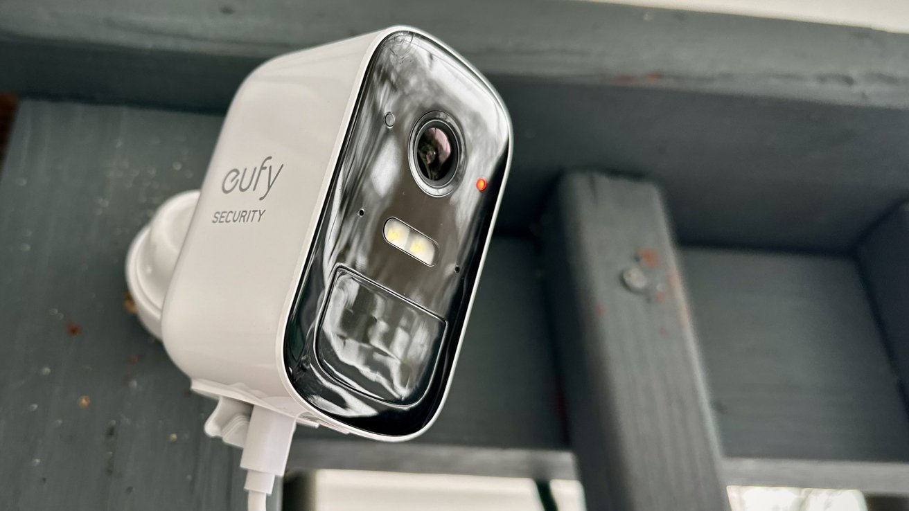 A close-up view of a mounted white Eufy security camera with a visible lens, LED light, and red indicator on a gray background.