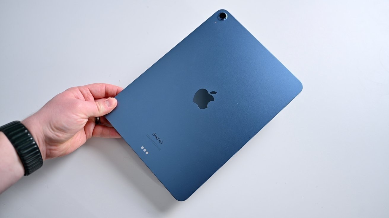 A hand holding a blue tablet with an apple logo visible on the back, against a light background.