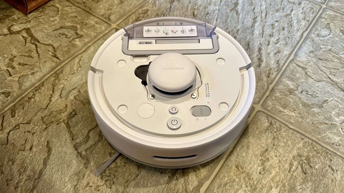 A robotic vacuum cleaner on a tiled floor with visible control buttons and a charging cord.