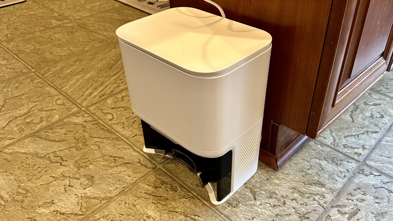 A white portable base with a black vent stands on a tiled floor next to wooden furniture.