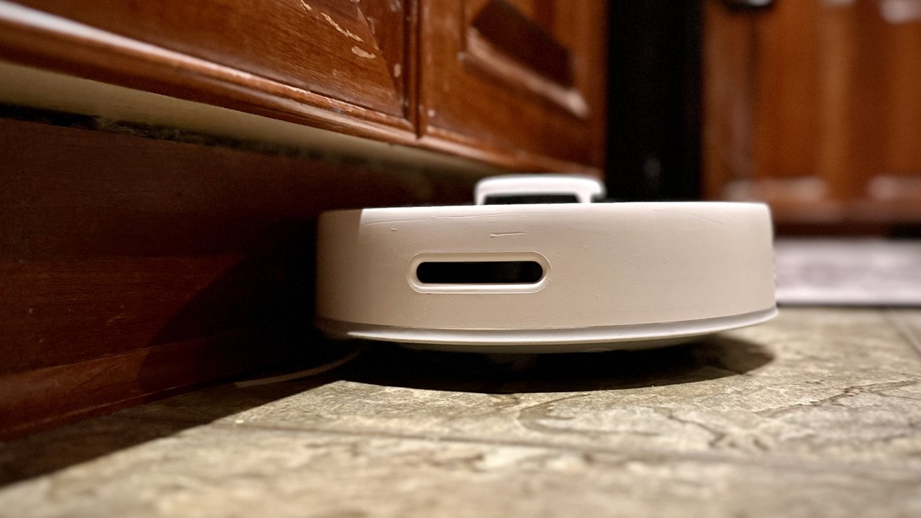 A robotic vacuum cleaner on a tiled floor near wooden furniture.