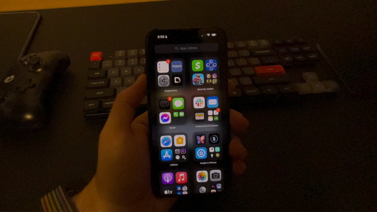 A low-resolution image of an iPhone display viewed through the Apple Vision Pro. A keyboard is in the background and the office appears to be dimly lit and warm tinted.