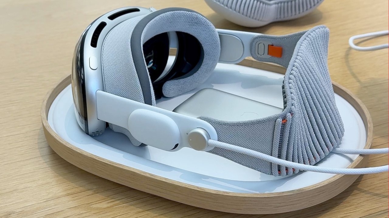 A close-up of a modern, gray and white virtual reality headset with cushioned straps resting on a circular stand on a wooden table.