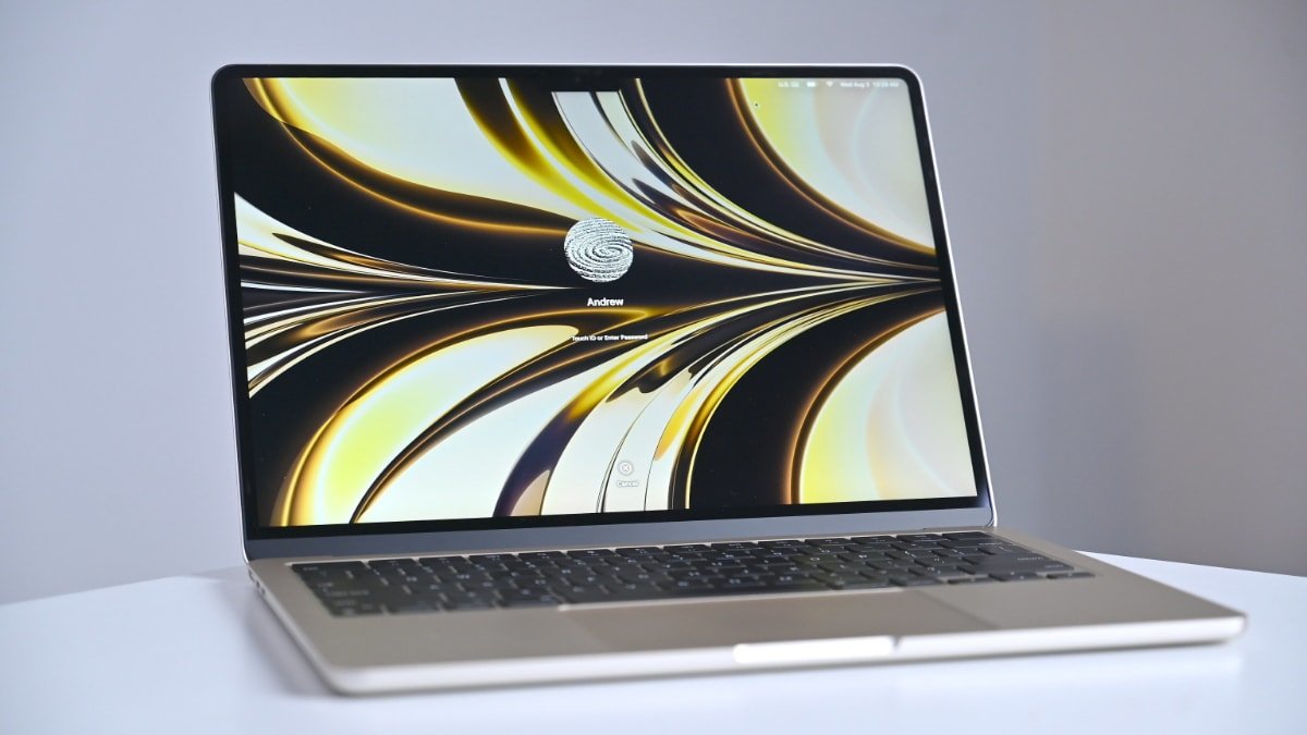 A MacBook Air on a white table displaying a vibrant abstract swirl wallpaper with a login prompt labeled 'Andrew' and a fingerprint icon.