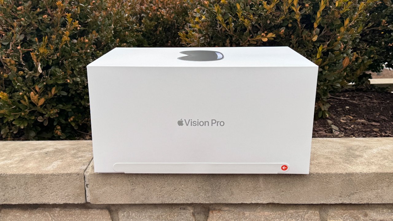 A white box with a logo and text 'Vision Pro' on a concrete ledge, green bushes in the background.