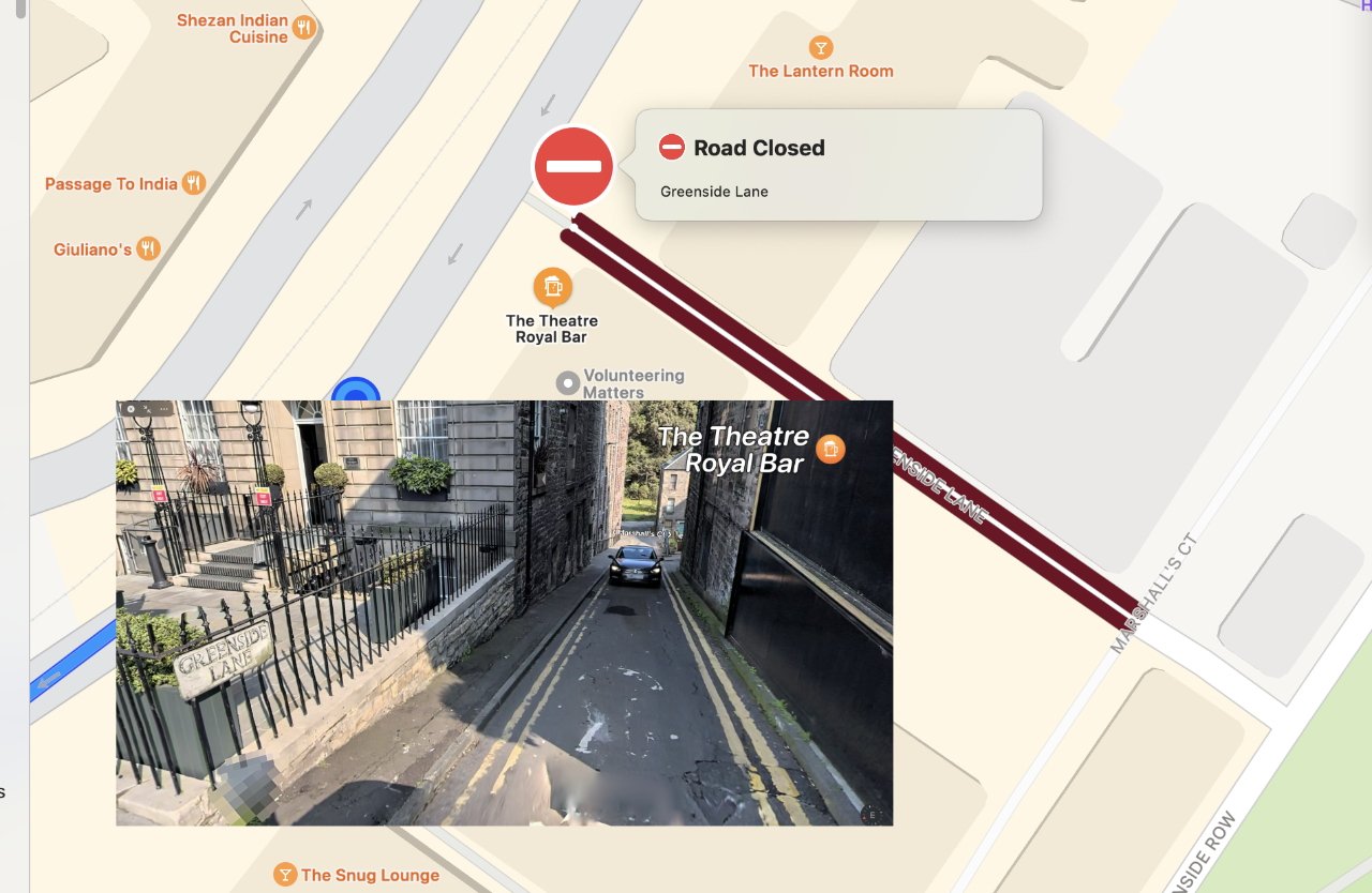 Street map overlaid with a photo perspective of a narrow lane between stone buildings and a car visible, showing a location named 