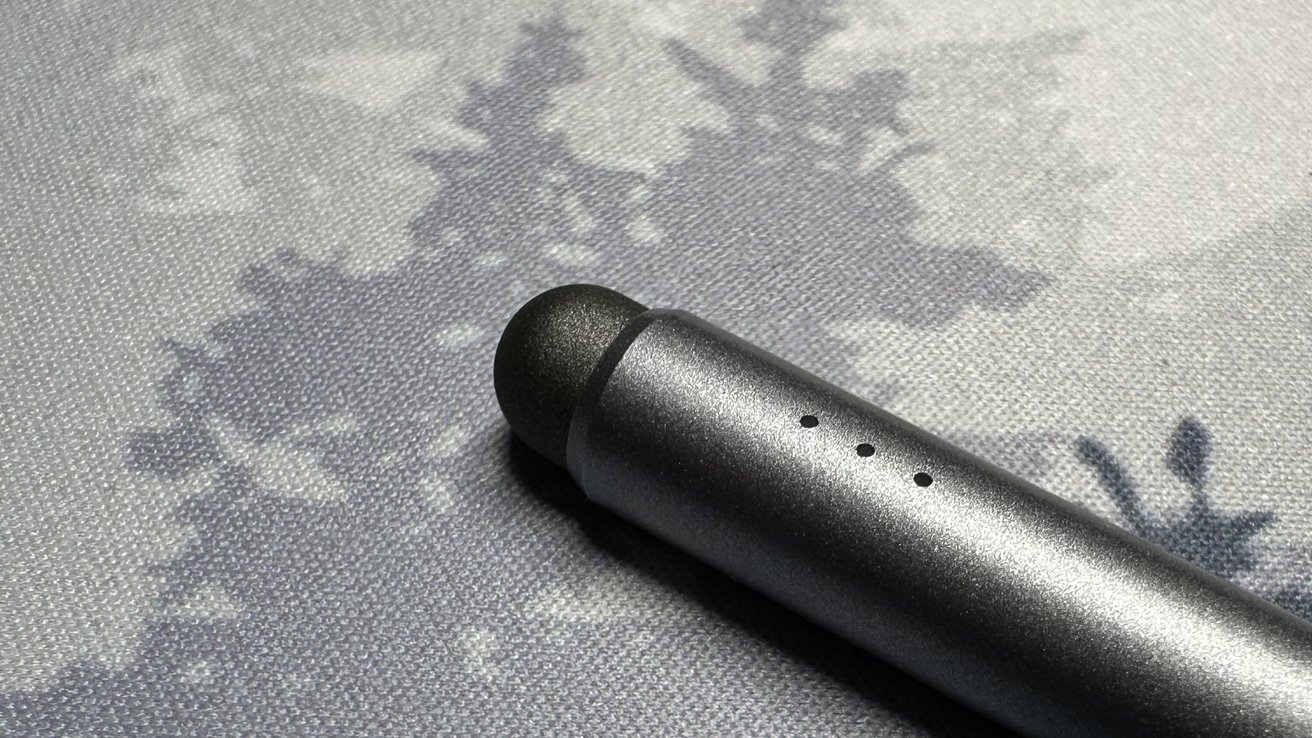 A close-up of a matte black digital pen resting on a textured grey surface with subtle floral patterns.