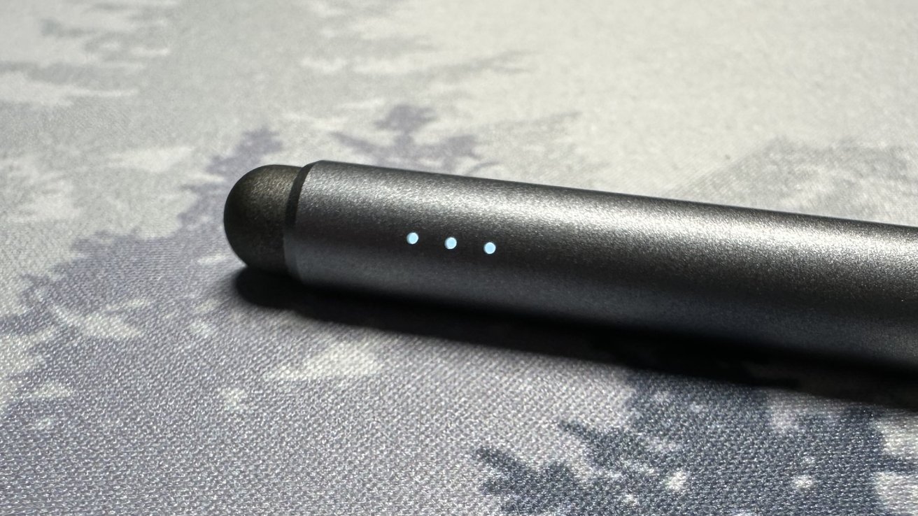 A black cylindrical object with three illuminated dots on its side, resting on a textured gray surface with faded patterns.