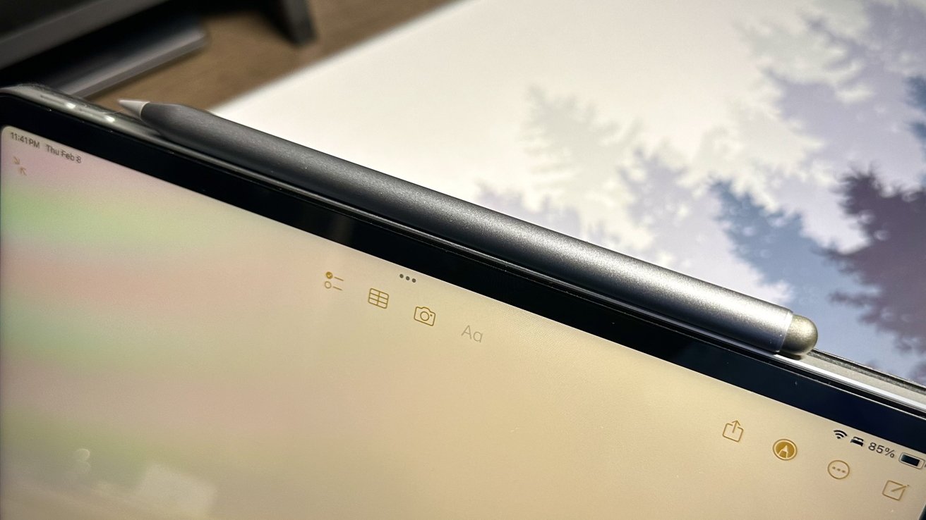 Close-up of an iPad with a stylus on top, displaying icons and battery status, reflecting clouds on the screen.