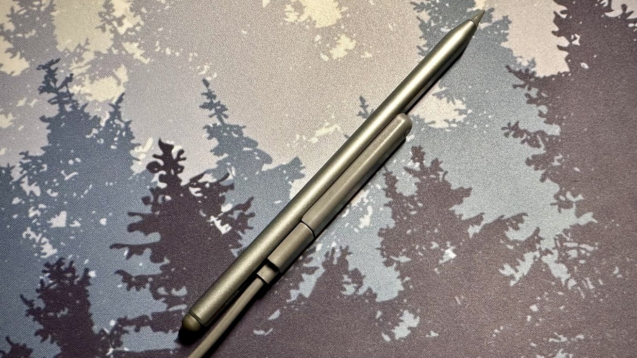 A sleek metallic pen diagonally placed over a backdrop with a tree silhouette pattern in shades of grey and white.