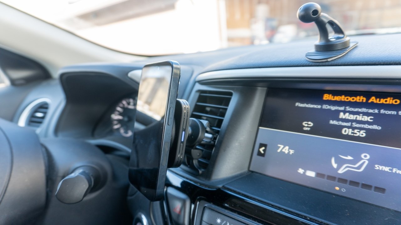 Car dashboard with a smartphone mounted on a suction holder displaying Bluetooth audio screen, air vents and control buttons visible.