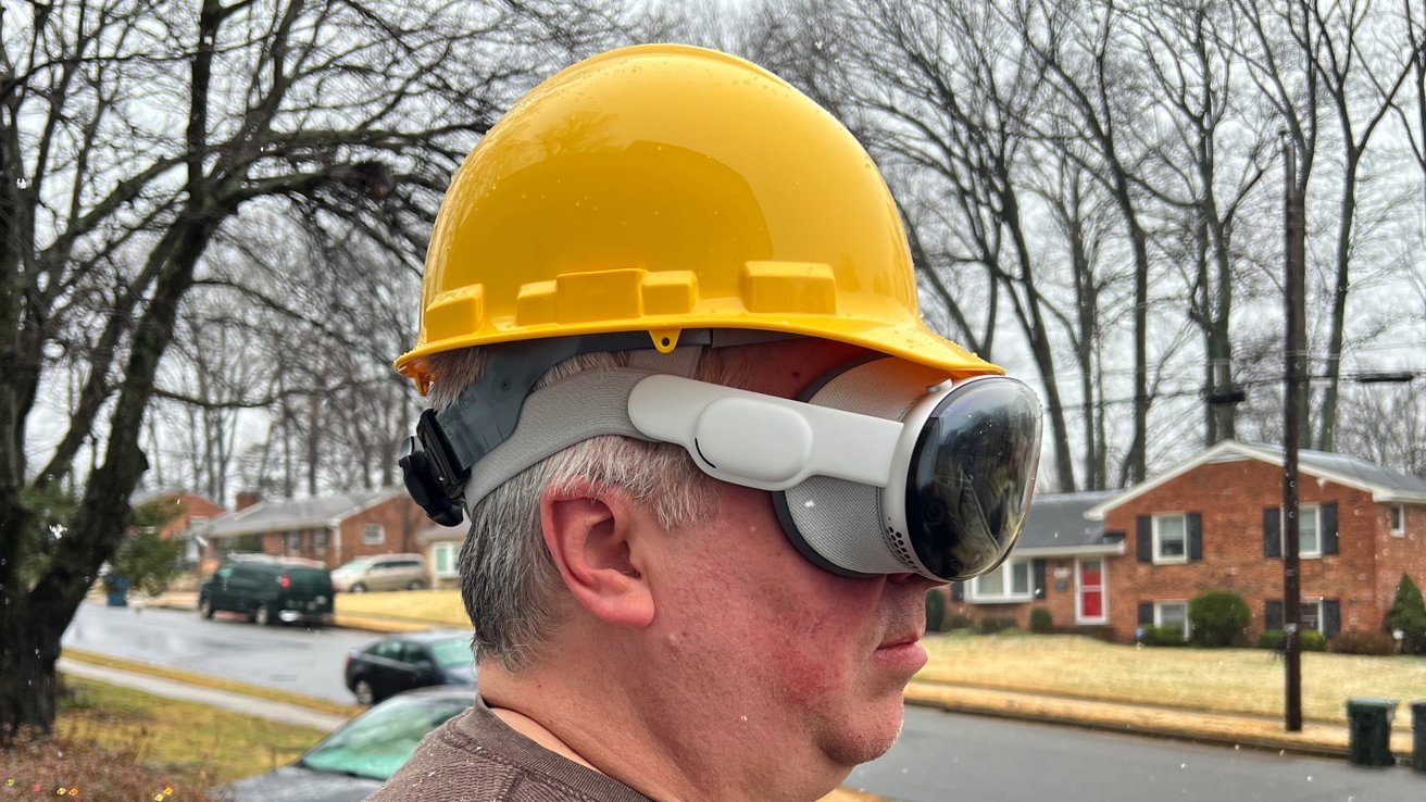 Person with a yellow hard hat and Apple Vision Pro against a residential street backdrop