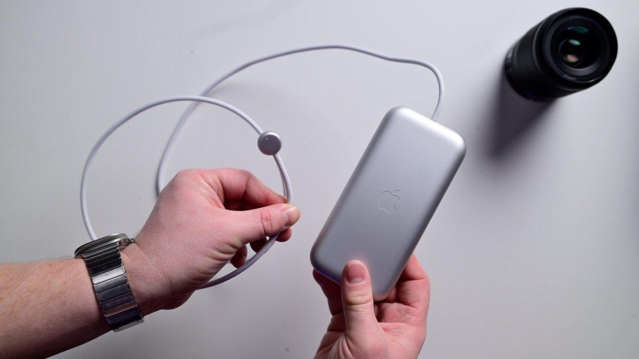 Hands holding the Apple Vision Pro silver power bank, with a camera lens in the background