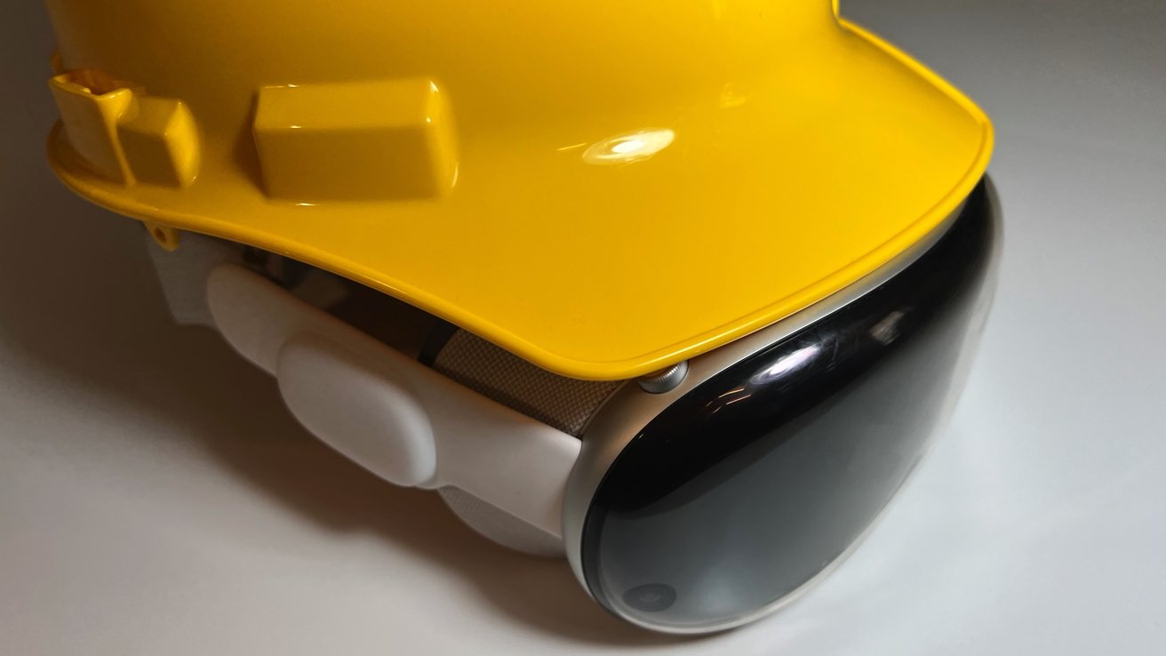 A bright yellow hard hat, on top of an Apple Vision Pro, resting on a white surface