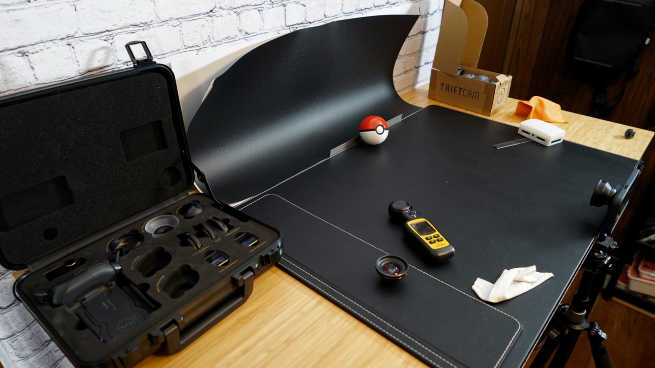 A photo table strewn with photography equipment like lenses, a light meter, and an iPhone on a tripod.