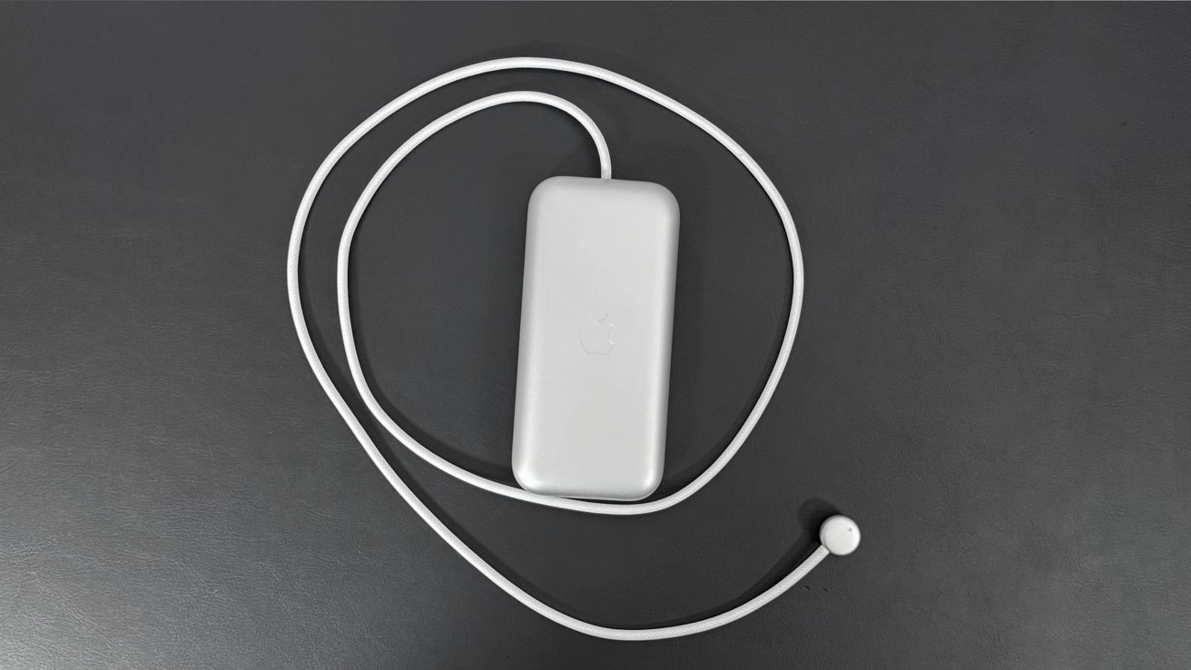 The Apple Vision Pro battery with its cable circling it on a black tabletop