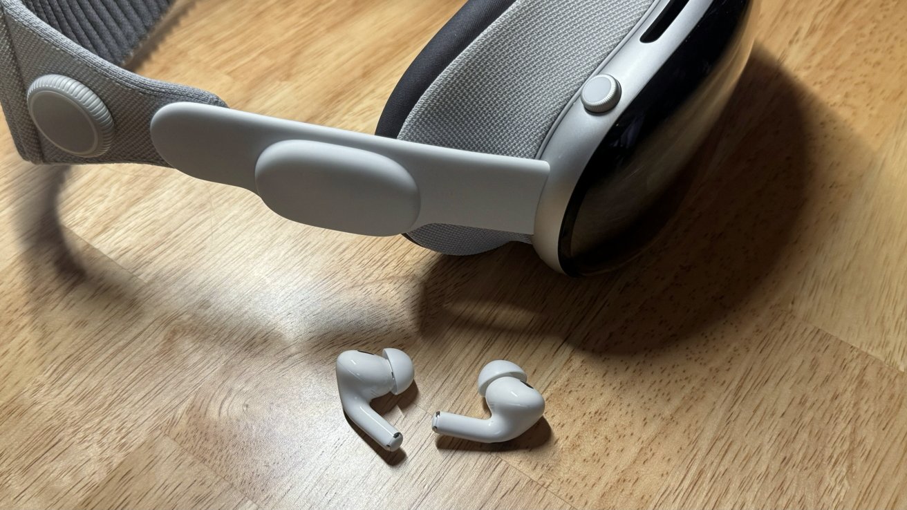 Apple Vision Pro on a desk next to two AirPods Pro earbuds
