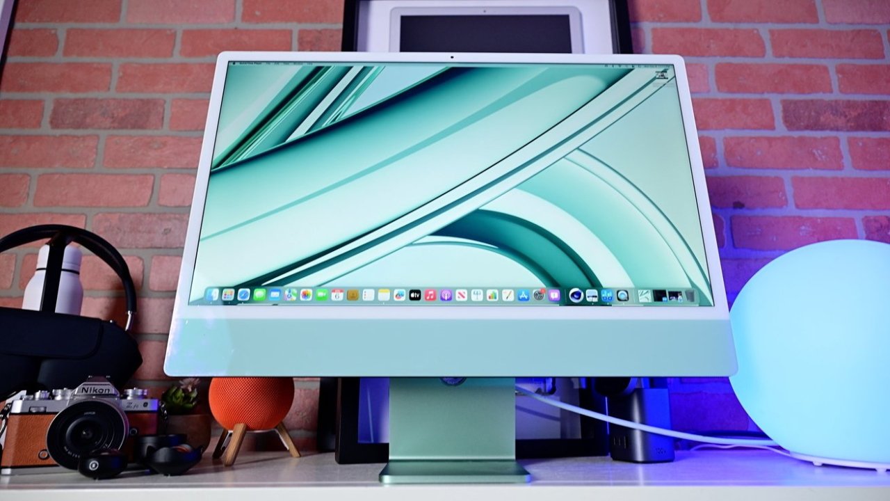 A desktop computer monitor displaying a colorful abstract wallpaper on a desk with various gadgets and ambient lighting.