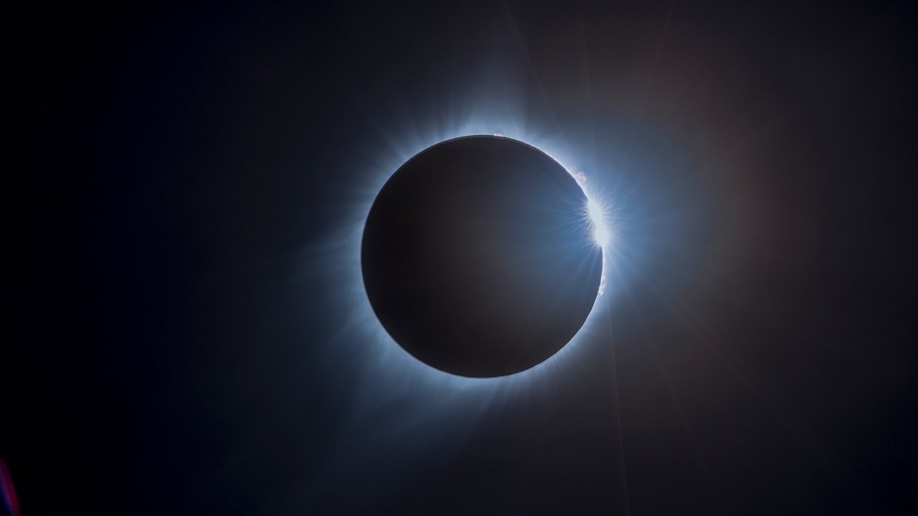 A solar eclipse with a diamond ring effect and corona visible around the silhouette of the moon against a dark sky.