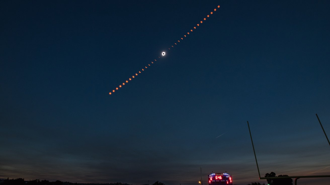 A time-lapse photo showing stages of a solar eclipse against a twilight sky over an electronic scoreboard.