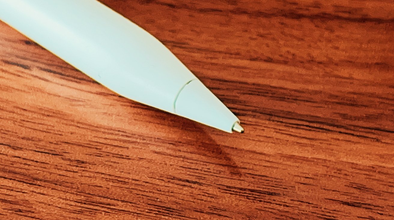 Close-up of a white pen tip against a wooden background with visible wood grain texture.