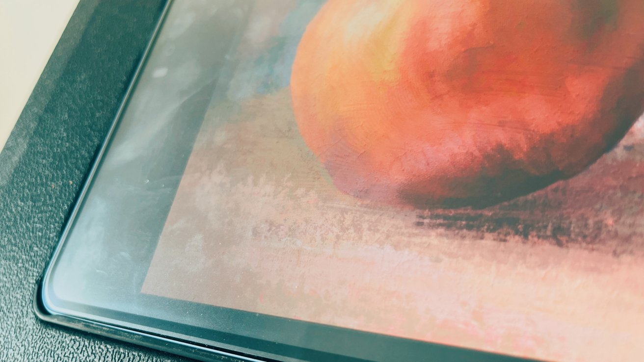 Painting of an apple with warm colors on a tablet screen, partially reflecting light.