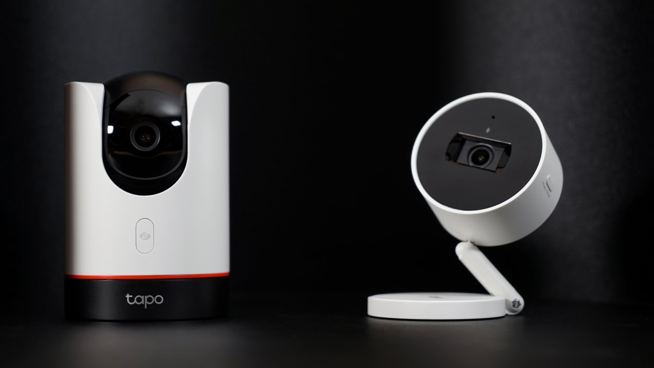 Two home security cameras on a table with a black background. Both are white, one has a swivel base and the other has an adjustable neck.