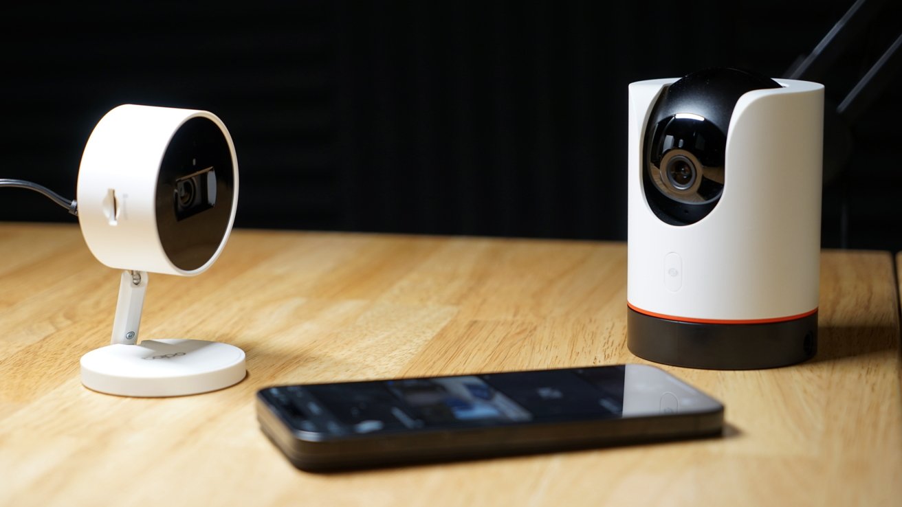 Two home security cameras on a desk next to an iPhone.