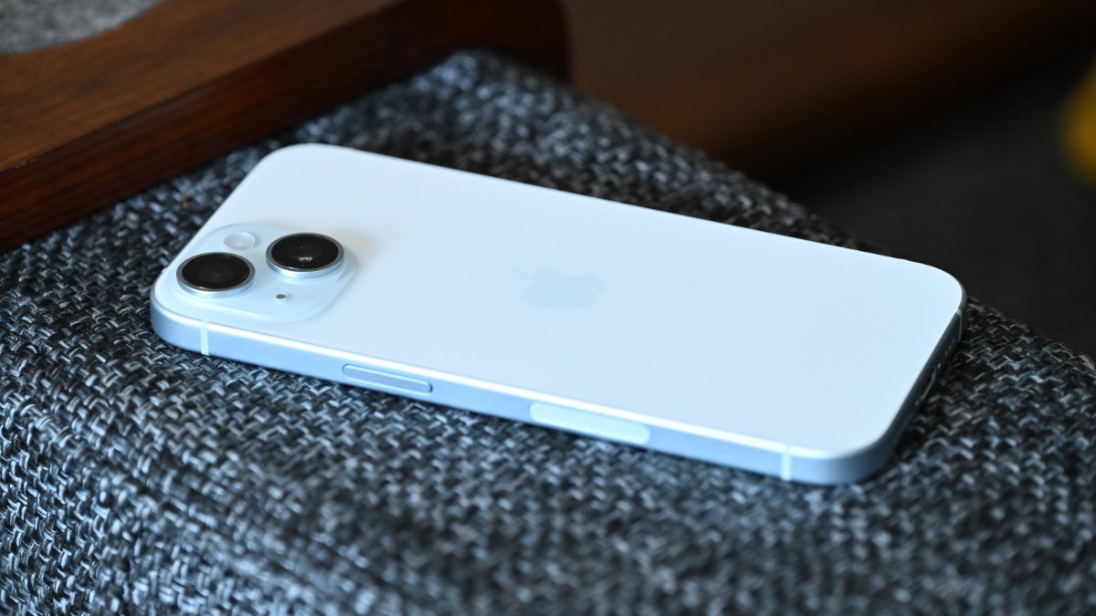 A blue iPhone 15 with dual cameras on a textured gray fabric surface.