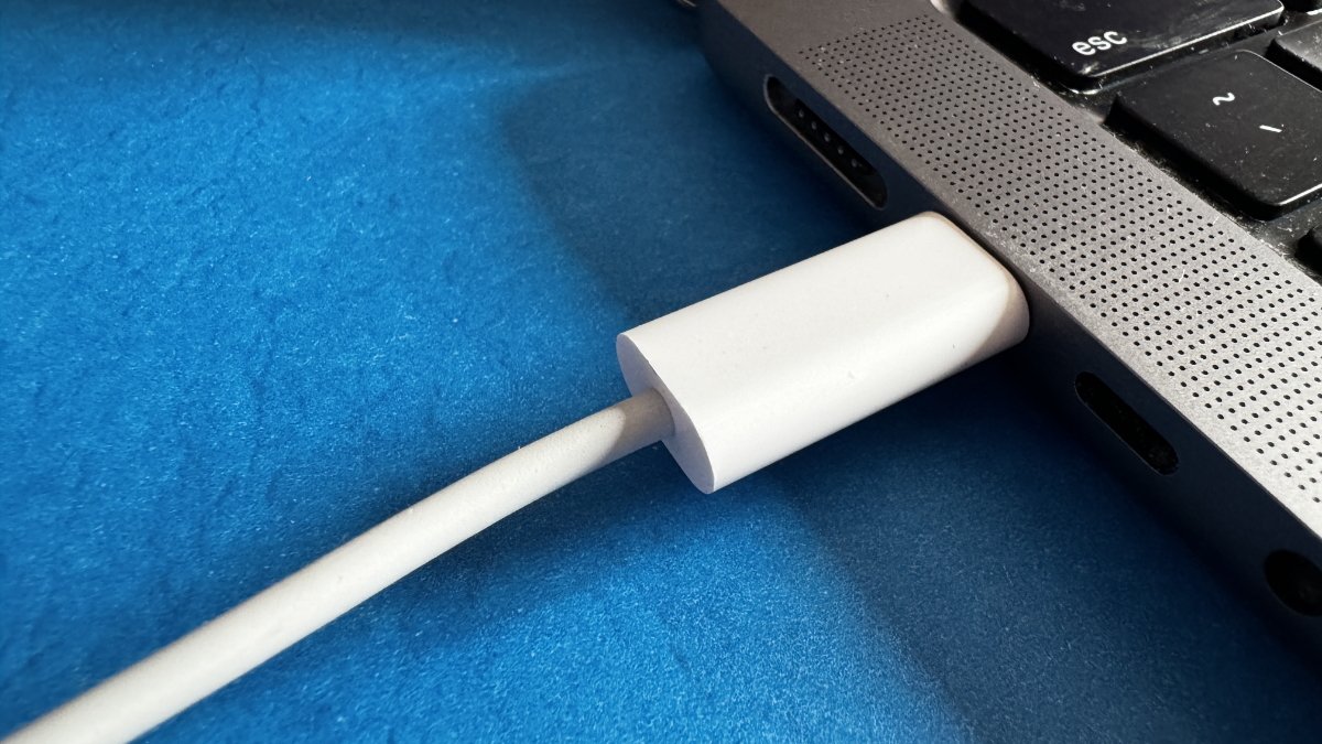 Close-up of a white dongle connected to a laptop, resting on a blue surface with the cable extending from it.