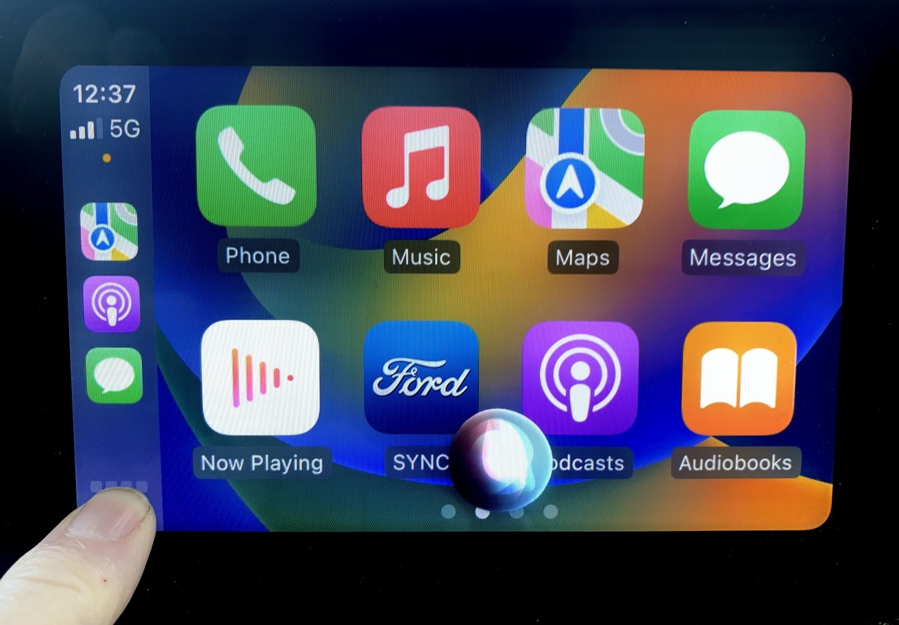 CarPlay menu displaying colorful app icons, including Phone, Music, Maps, and Messages, with a reflection on the screen.