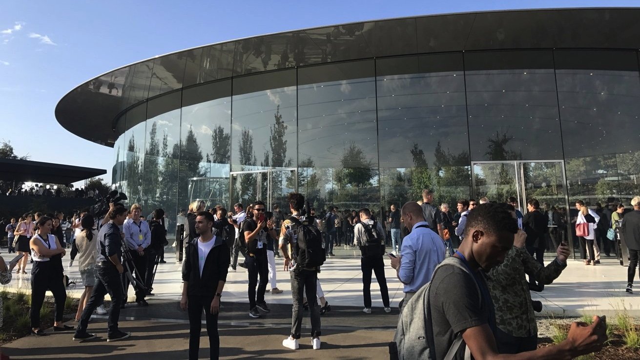 Group of people outside Steve Jobs Theater on a sunny day with some using smartphones.