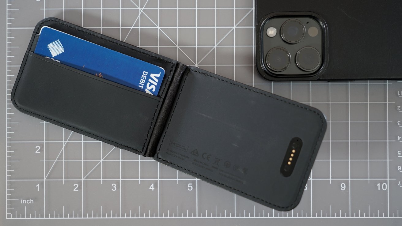 The Loc8 wallet opened with a blue Visa card on the left and a charging port on the right. An iPhone camera is in the corner of the photo.