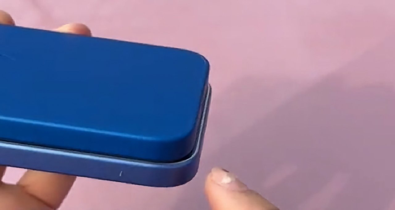 Close-up of a hand holding a blue phone with a clear protective case against a pink background.
