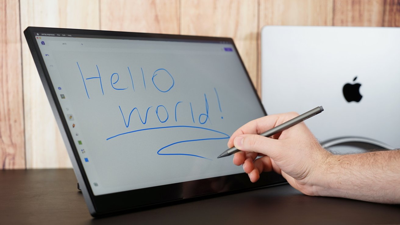 A portable monitor with the text 'hello world' written. A hand holding a stylus is visible.