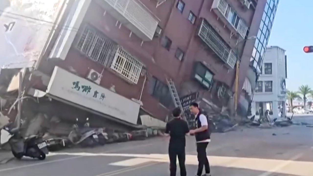 A tilting building on the verge of collapse with debris scattered, and two people observing the damage on a street.