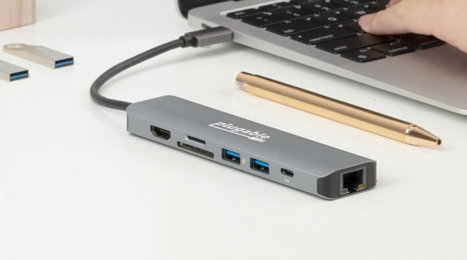 A USB-C hub connected to a laptop with various ports visible, placed on a desk next to a pen.