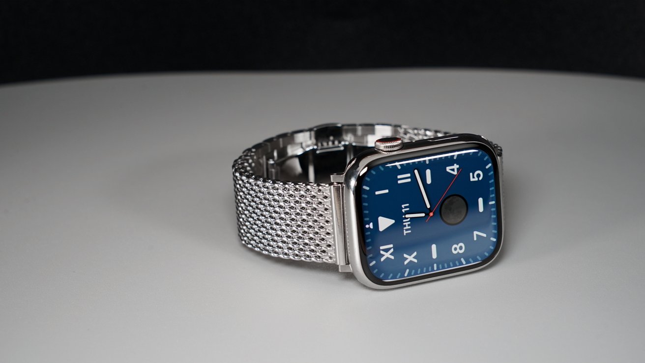 Stainless steel Apple Watch Series 9 with a blue face and large numbers on a Milanese link bracelet against a black background.