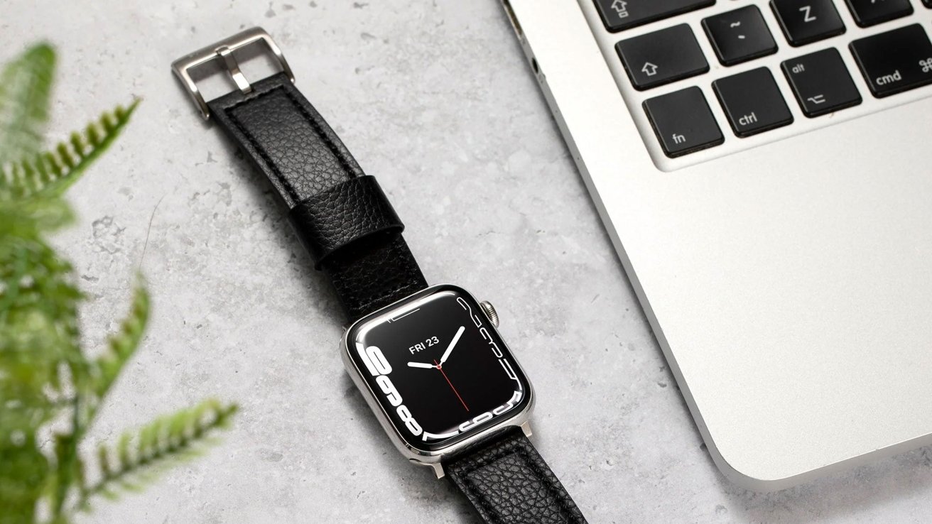 Apple Watch with Buck and Band leather band next to a MacBook keyboard on a marble surface, with a plant in soft focus.