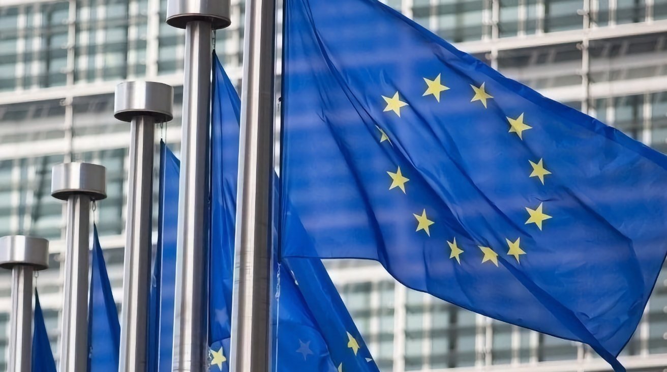 European Union flags fluttering with a backdrop of modern glass building facades.