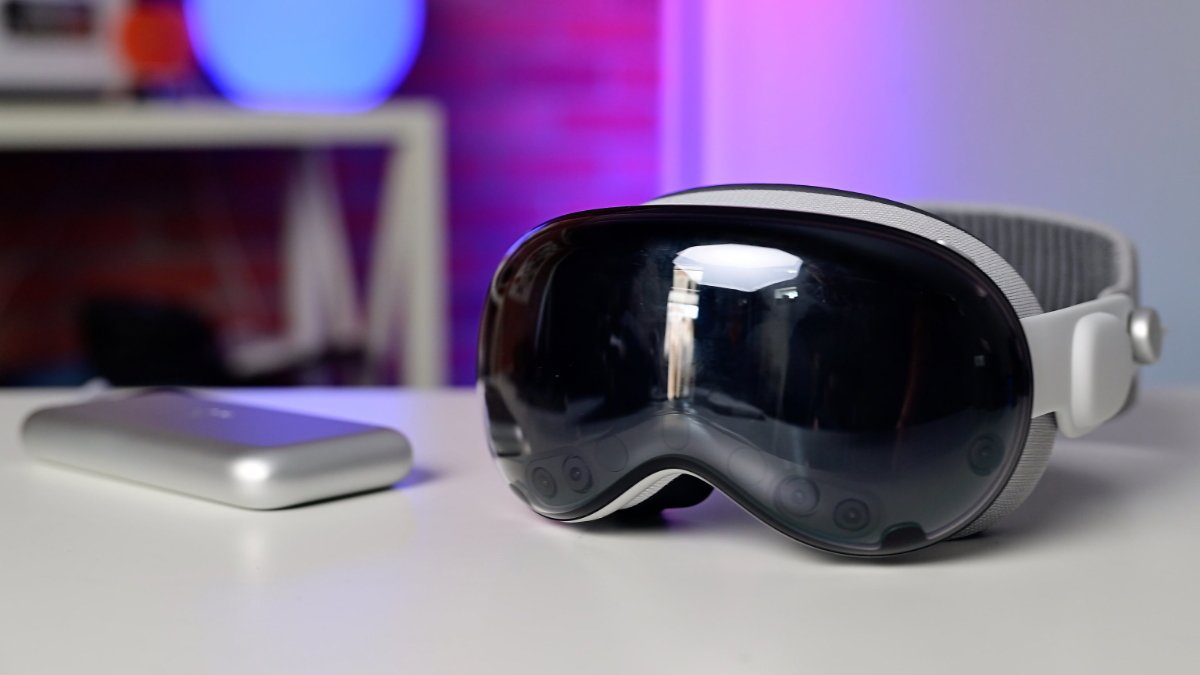 An Apple Vision Pro headset on a desk with colorful lighting in the background.