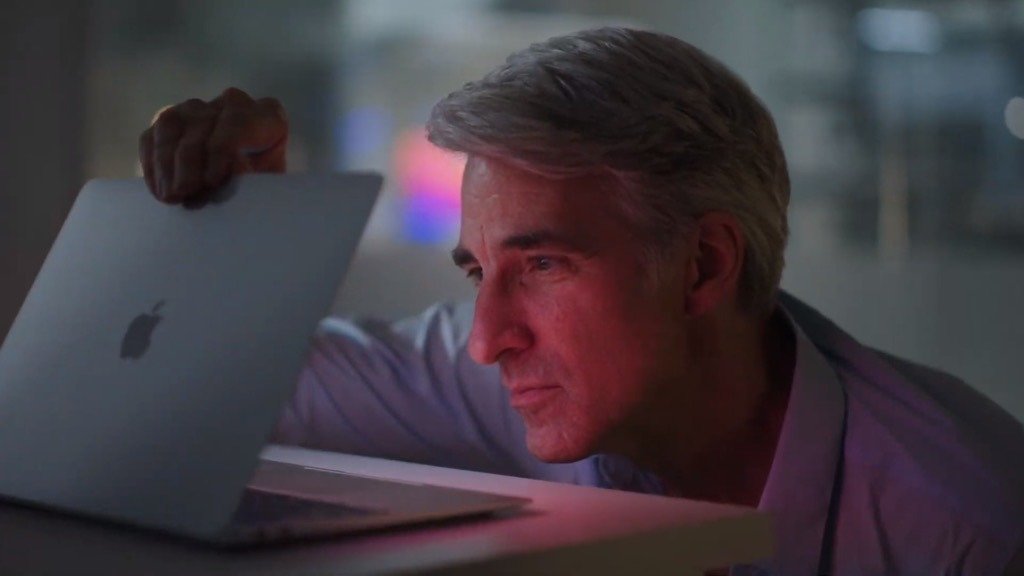 Mature man with gray hair looking intently at a glowing laptop screen, slightly smiling, in a dimly lit room.