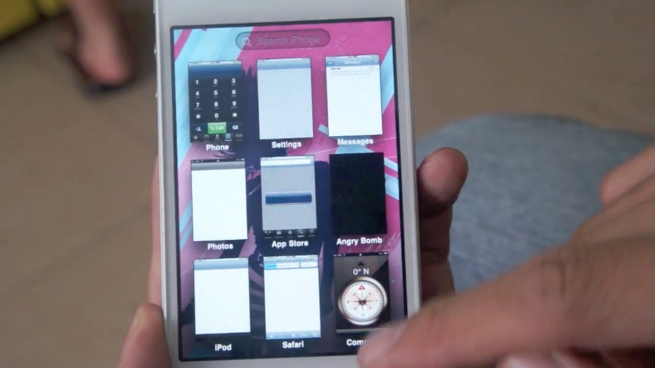 Hand holding a smartphone displaying various apps with a pink background.